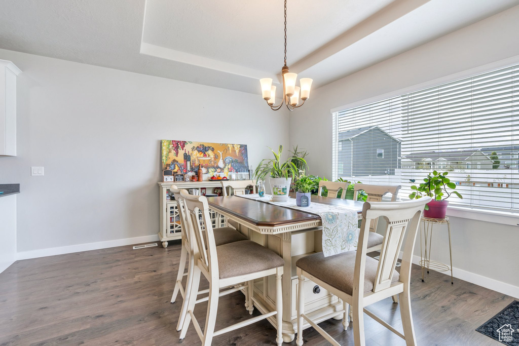 Dining space with a chandelier, wood finished floors, baseboards, and a tray ceiling