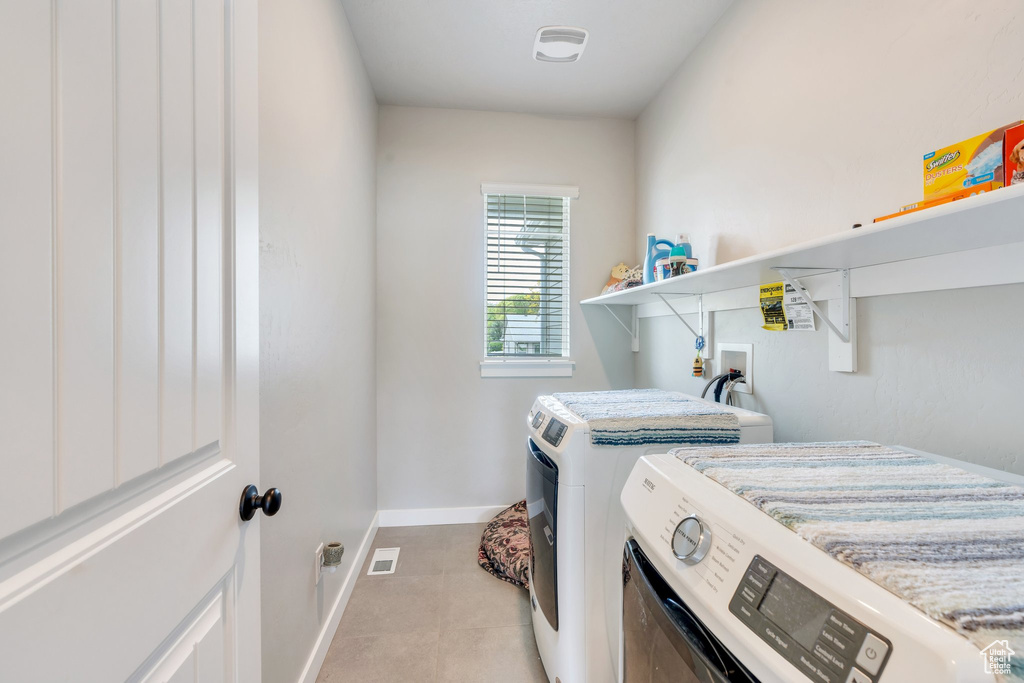 Clothes washing area featuring washing machine and dryer, light tile patterned flooring, and baseboards