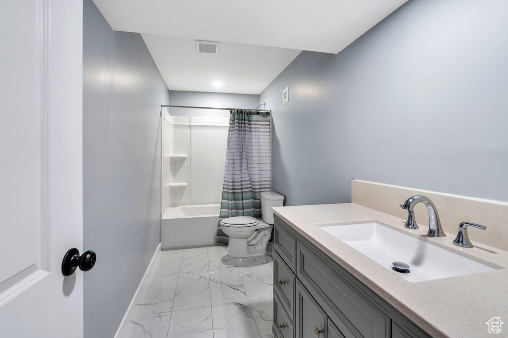 Full bathroom with toilet, marble look tiles, shower / bath combo, vanity, and baseboards