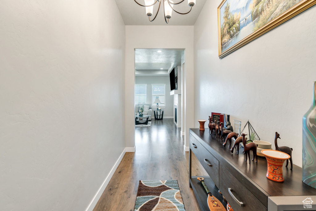 Hallway featuring wood finished floors, a chandelier, and baseboards