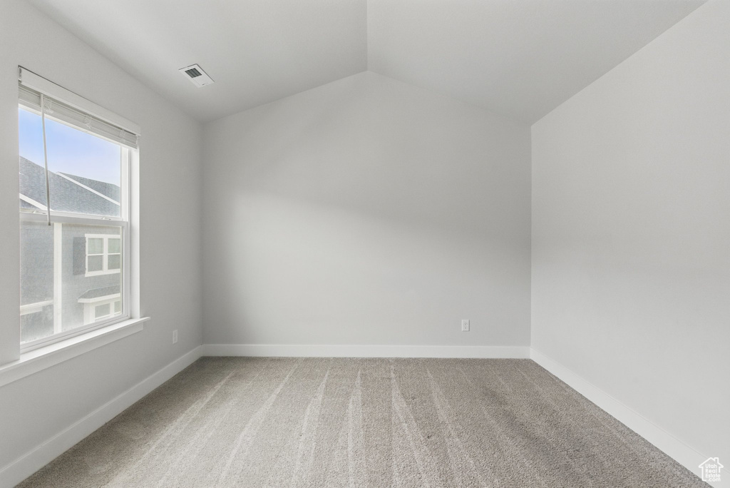 Empty room with light colored carpet, vaulted ceiling, and baseboards