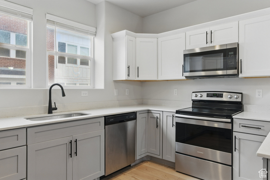 Kitchen with appliances with stainless steel finishes, a sink, light wood-style flooring, light countertops, and white cabinets