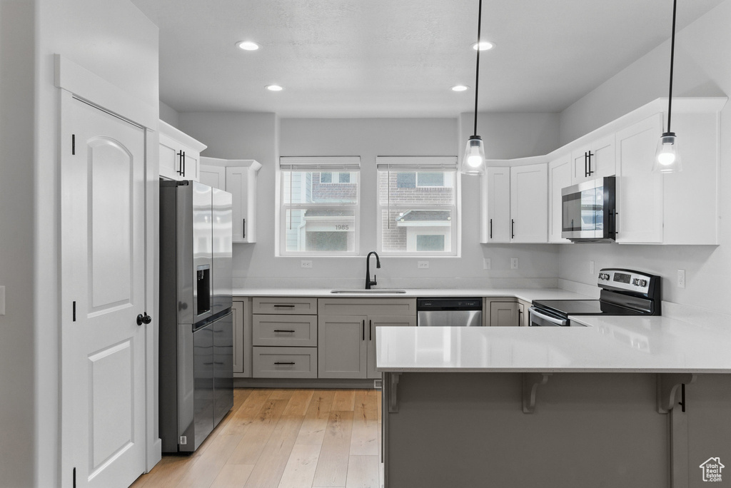 Kitchen with appliances with stainless steel finishes, a sink, a peninsula, light wood finished floors, and light countertops