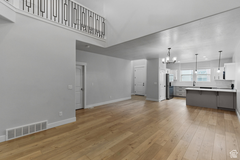 Unfurnished living room featuring a chandelier, light wood finished floors, baseboards, a sink, and a towering ceiling