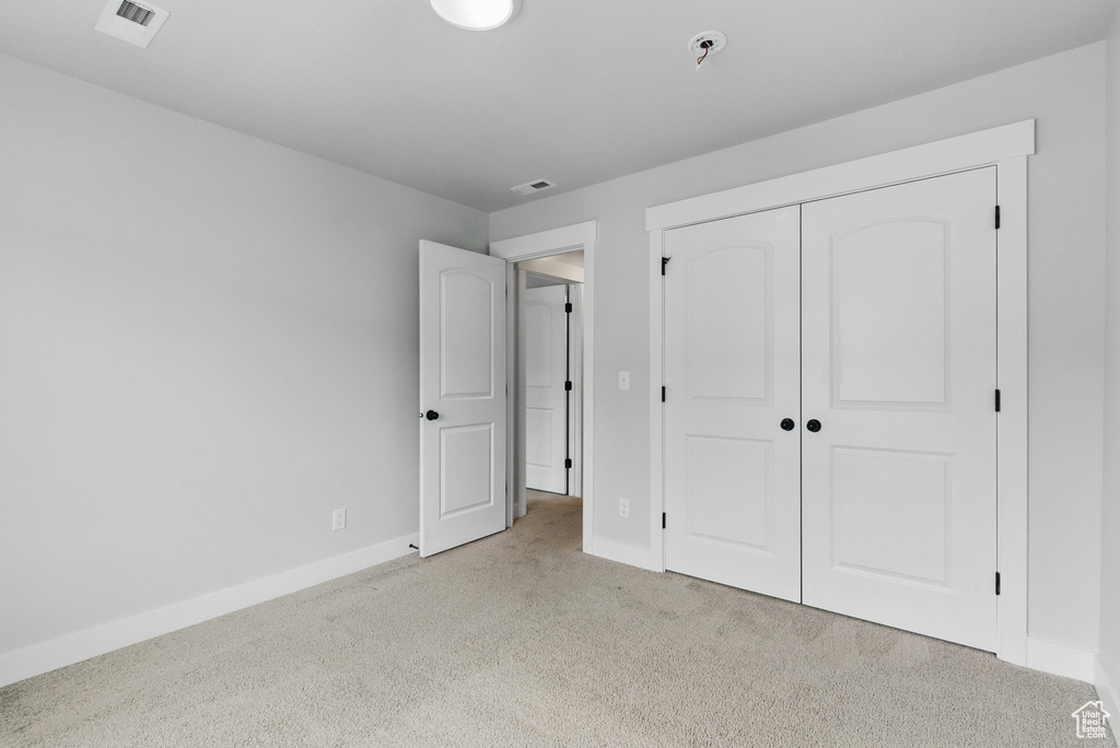 Unfurnished bedroom with light carpet, baseboards, and a closet