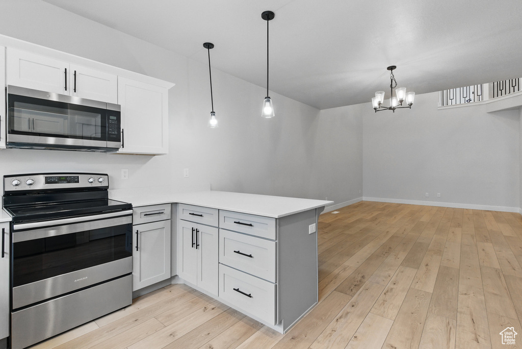 Kitchen featuring appliances with stainless steel finishes, a peninsula, a chandelier, light countertops, and light wood-type flooring