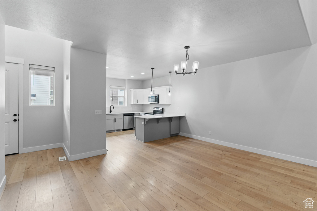 Kitchen with appliances with stainless steel finishes, a sink, a peninsula, a chandelier, and baseboards