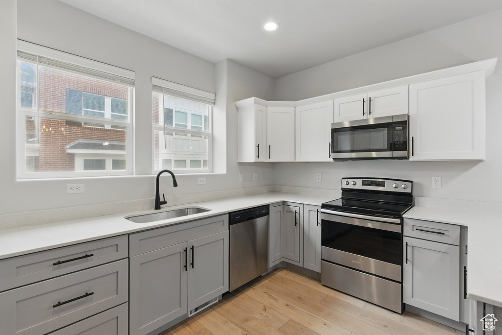Kitchen featuring stainless steel appliances, a sink, light wood-style flooring, gray cabinetry, and light countertops