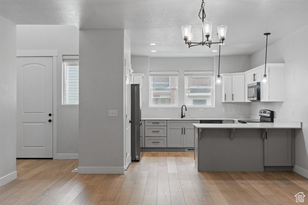 Kitchen with appliances with stainless steel finishes, a sink, a peninsula, gray cabinetry, and a chandelier