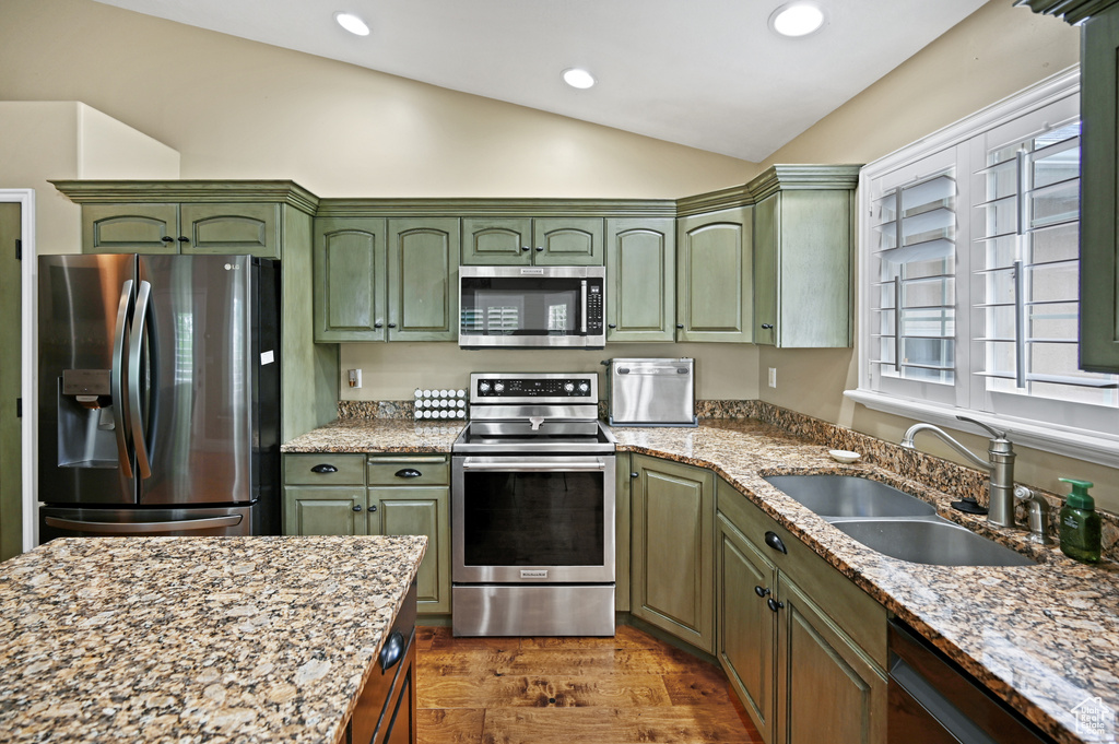 Kitchen featuring stainless steel appliances, green cabinetry, a sink, vaulted ceiling, and dark wood-style flooring