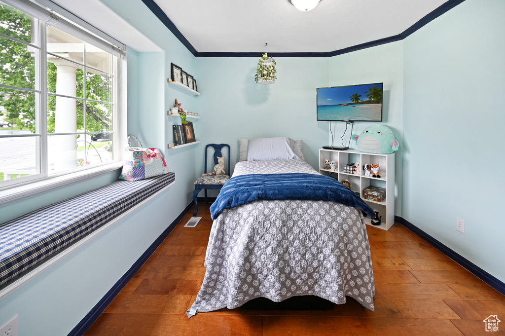 Bedroom with multiple windows, ornamental molding, baseboards, and wood finished floors