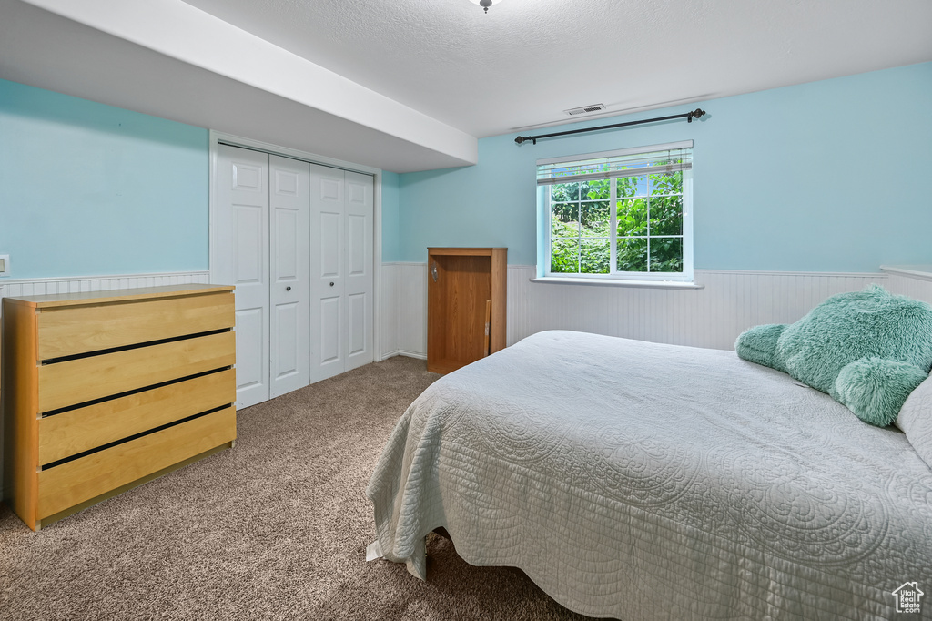 Carpeted bedroom featuring a wainscoted wall and a closet