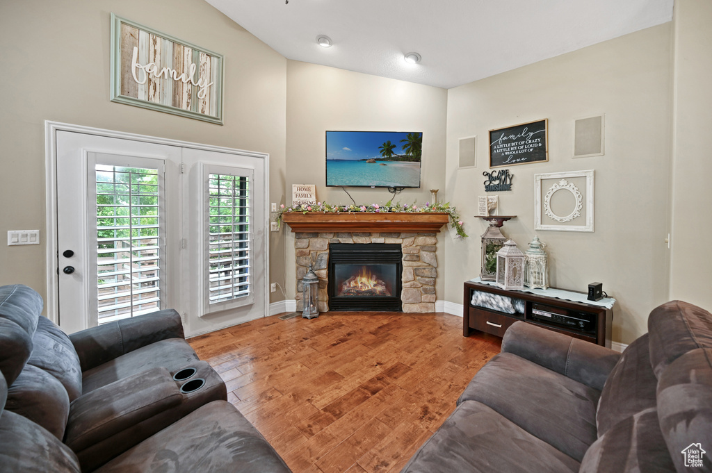 Living area featuring a stone fireplace, wood finished floors, baseboards, and a towering ceiling