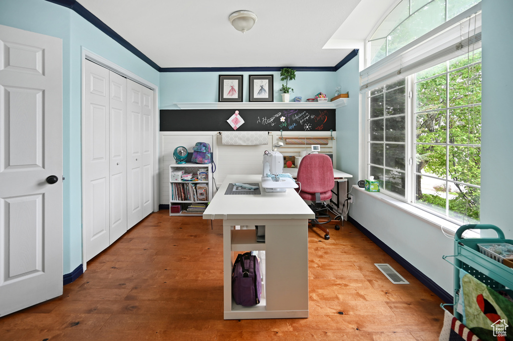 Office space with wood finished floors, plenty of natural light, baseboards, and ornamental molding