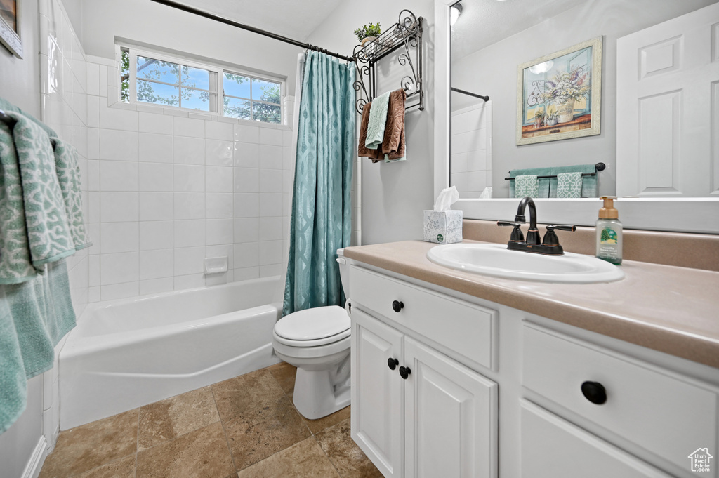 Bathroom with toilet, shower / tub combo with curtain, vanity, and stone finish flooring