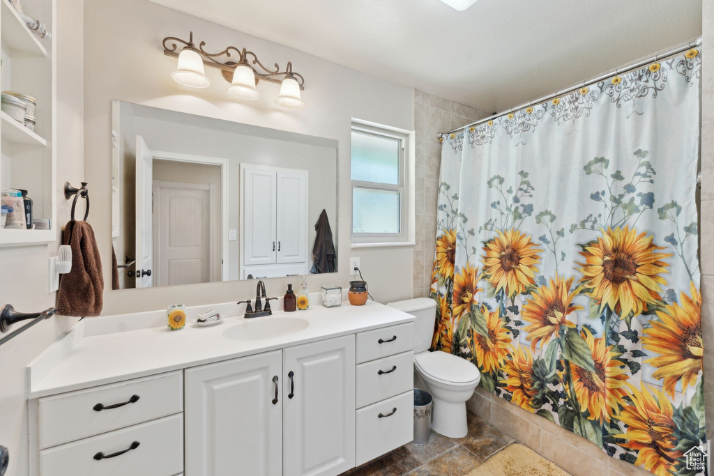 Bathroom with toilet, vanity, a shower with curtain, and stone finish flooring