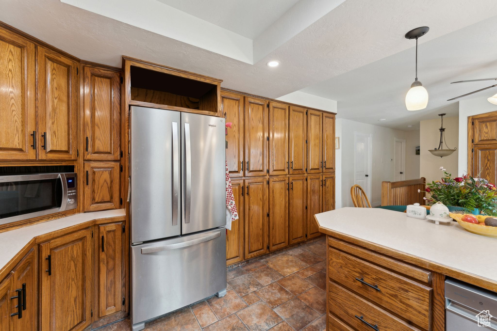 Kitchen featuring appliances with stainless steel finishes, brown cabinets, stone finish flooring, light countertops, and decorative light fixtures