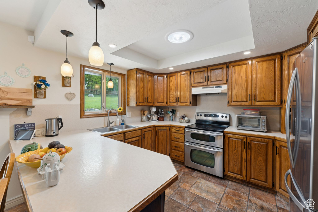 Kitchen with stainless steel appliances, a sink, a raised ceiling, brown cabinets, and light countertops