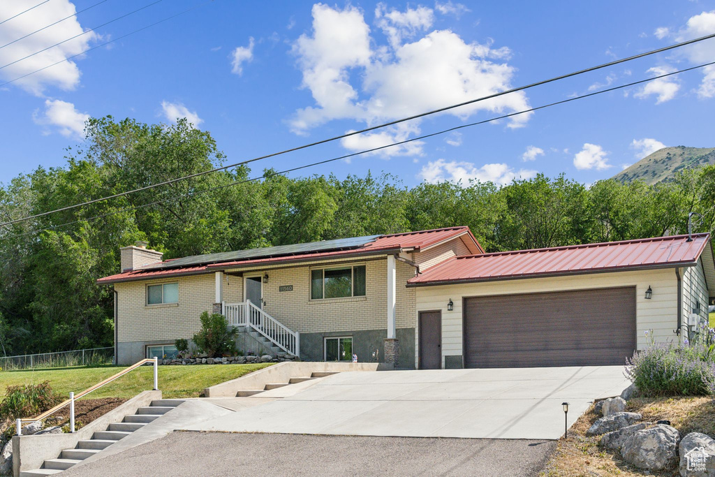 View of front of home featuring driveway, an attached garage, solar panels, metal roof, and stairs