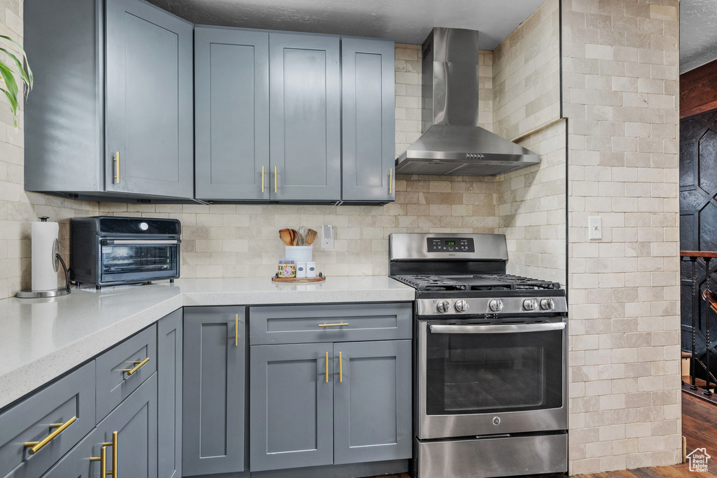 Kitchen with stainless steel gas stove, wall chimney exhaust hood, light countertops, and backsplash