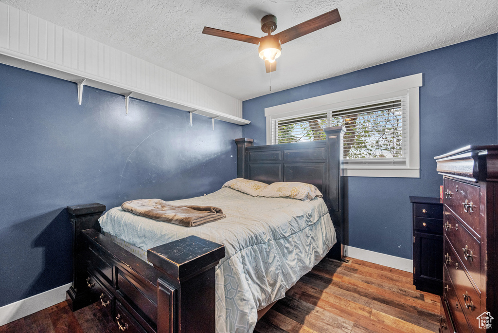 Bedroom with a textured ceiling, wood finished floors, baseboards, and ceiling fan