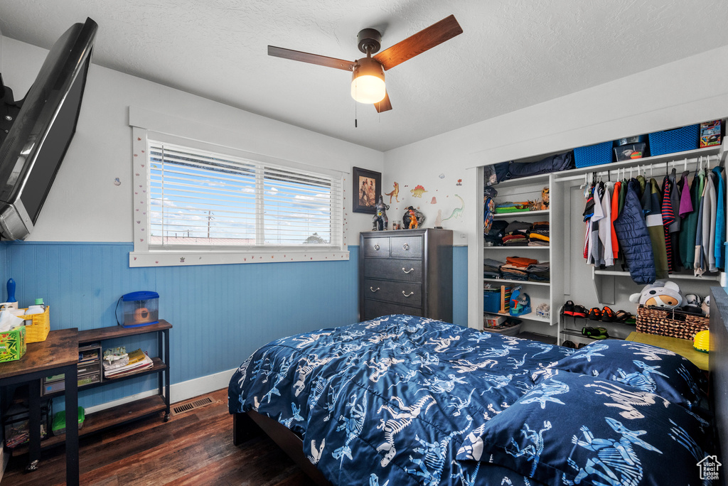 Bedroom featuring wood finished floors, wainscoting, a closet, ceiling fan, and baseboards