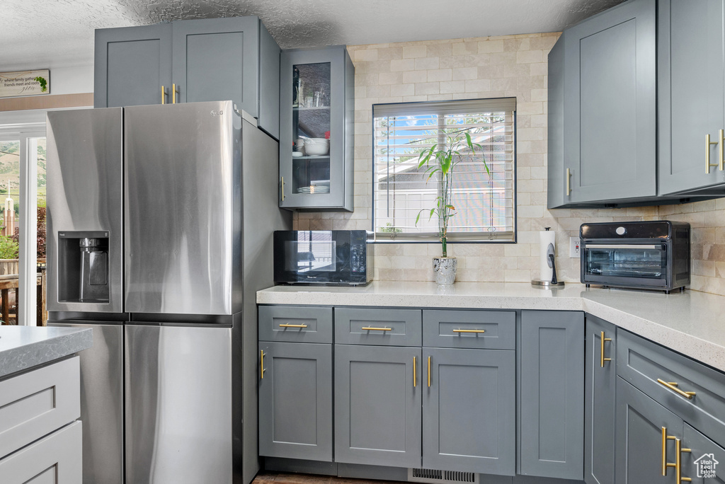 Kitchen featuring stainless steel fridge, black microwave, light countertops, and a textured ceiling