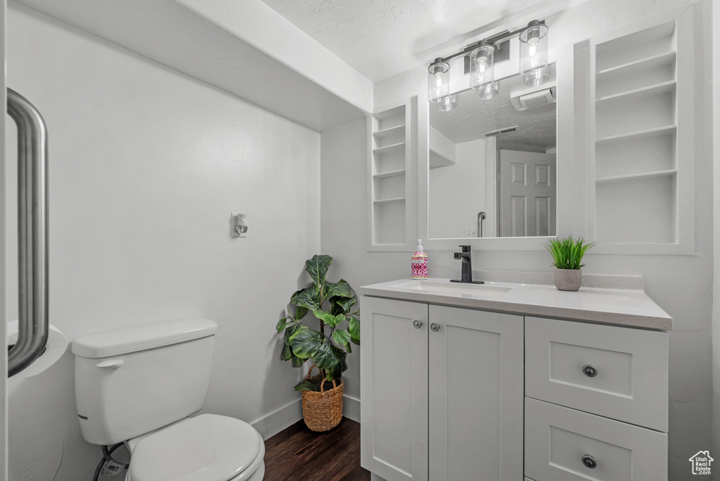 Bathroom with wood finished floors, toilet, baseboards, vanity, and a textured ceiling