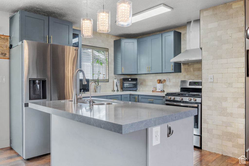 Kitchen with wall chimney exhaust hood, stainless steel appliances, a sink, dark wood finished floors, and decorative backsplash