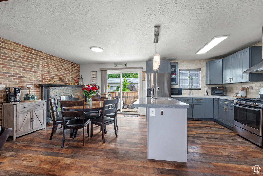 Kitchen with stainless steel appliances, dark wood finished floors, brick wall, a textured ceiling, and decorative light fixtures