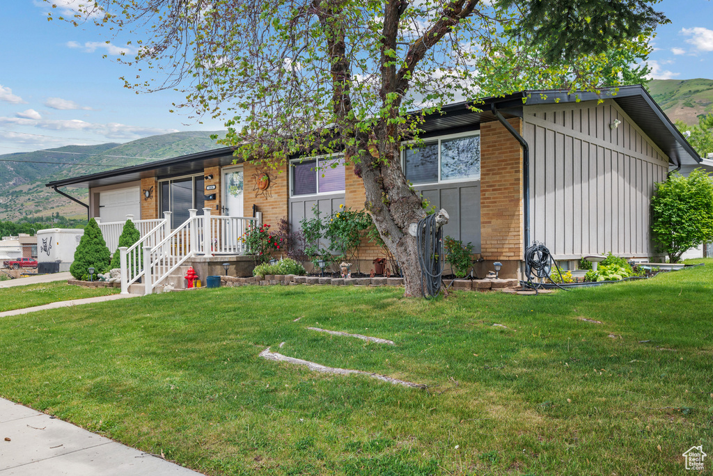 View of front of home featuring board and batten siding, a mountain view, a front lawn, and brick siding