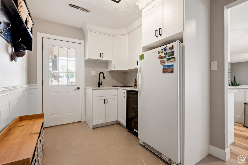 Kitchen featuring freestanding refrigerator, light countertops, a sink, white cabinets, and backsplash