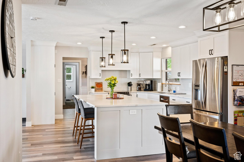 Kitchen featuring stainless steel refrigerator with ice dispenser, light wood finished floors, white cabinetry, backsplash, and recessed lighting