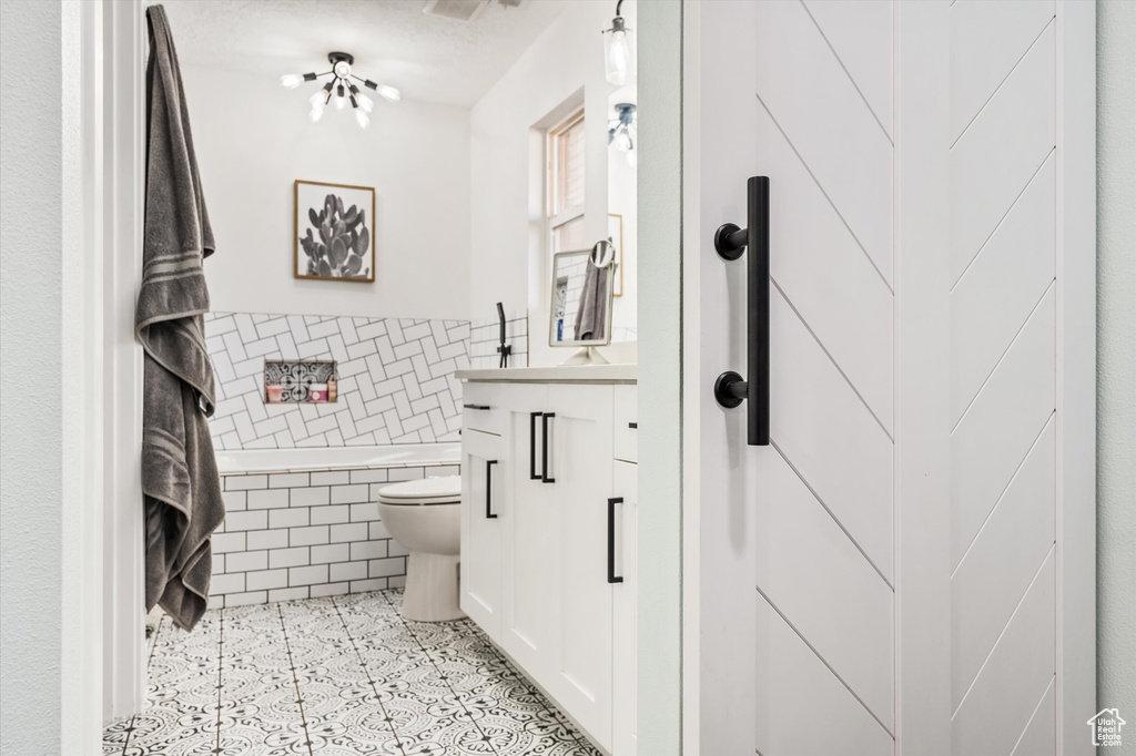 Full bathroom with tile walls, toilet, tiled bath, vanity, and wainscoting