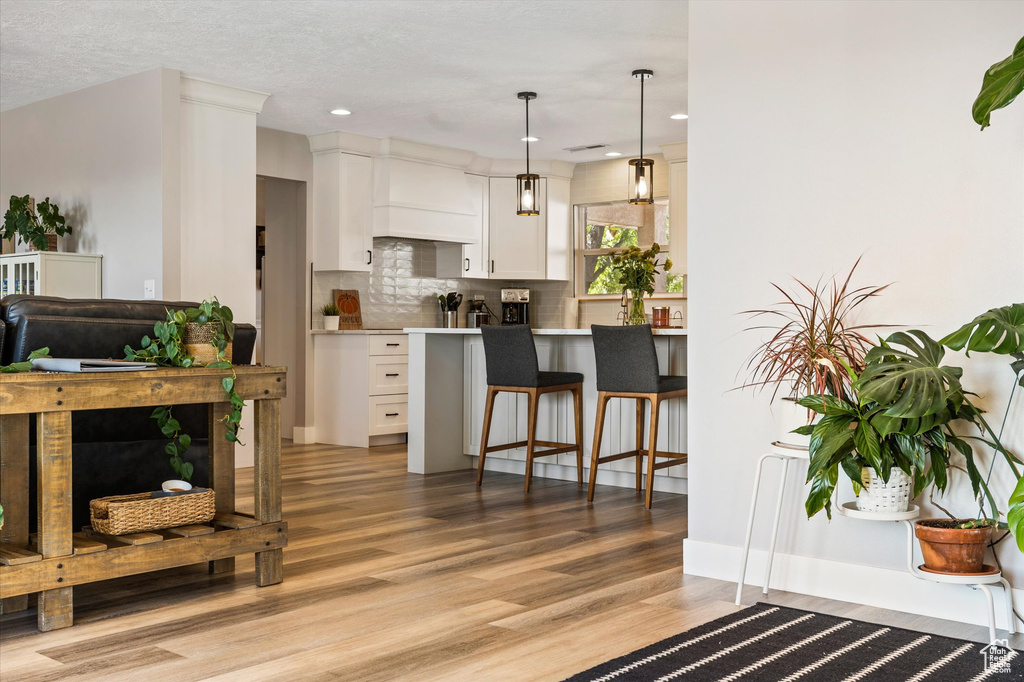 Kitchen with premium range hood, a breakfast bar, light wood-style flooring, white cabinetry, and decorative backsplash