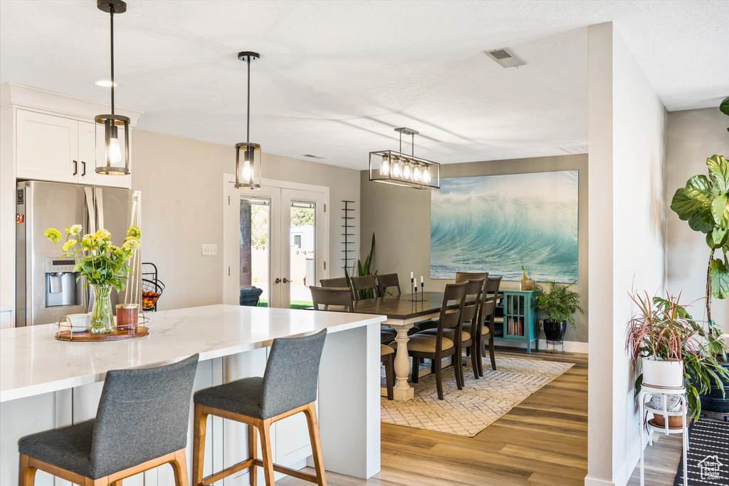 Kitchen featuring stainless steel fridge, light wood-style flooring, a breakfast bar, white cabinets, and pendant lighting