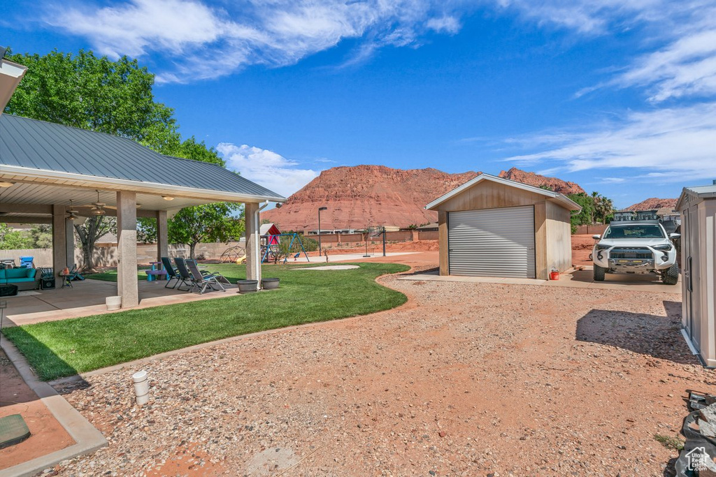 View of yard featuring a playground, ceiling fan, an outdoor structure, a mountain view, and a patio area