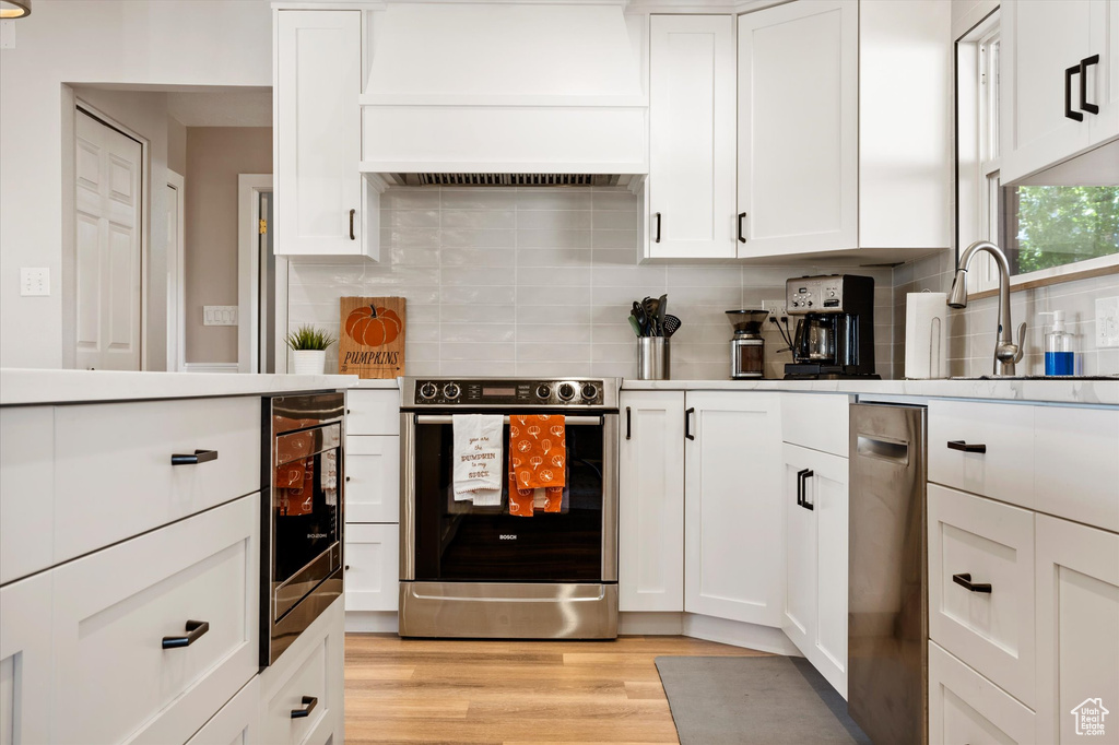 Kitchen featuring stainless steel appliances, custom range hood, and white cabinets
