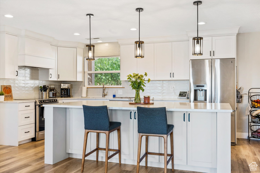 Kitchen featuring appliances with stainless steel finishes, custom range hood, a kitchen island, white cabinets, and recessed lighting