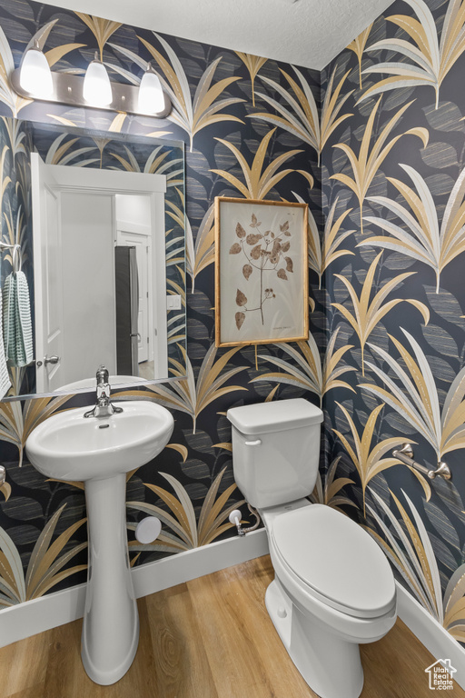 Bathroom with wallpapered walls, baseboards, toilet, and wood finished floors