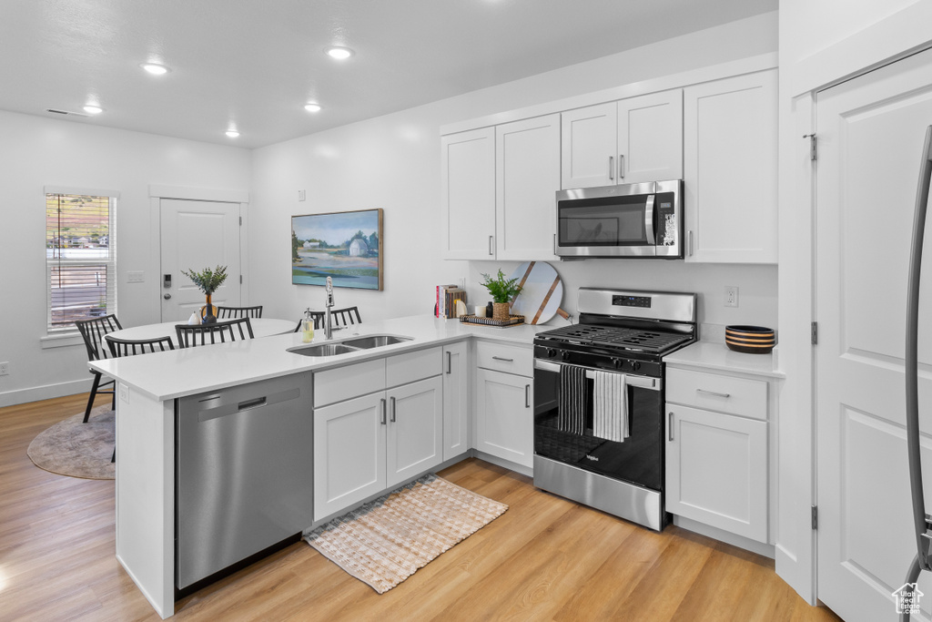Kitchen featuring appliances with stainless steel finishes, a sink, a peninsula, light wood-type flooring, and light countertops