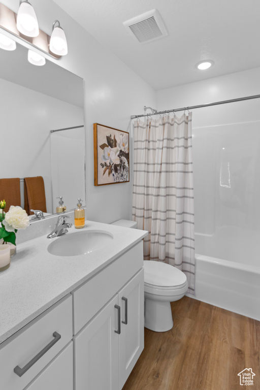 Bathroom featuring wood finished floors, toilet, vanity, and shower / tub combo with curtain