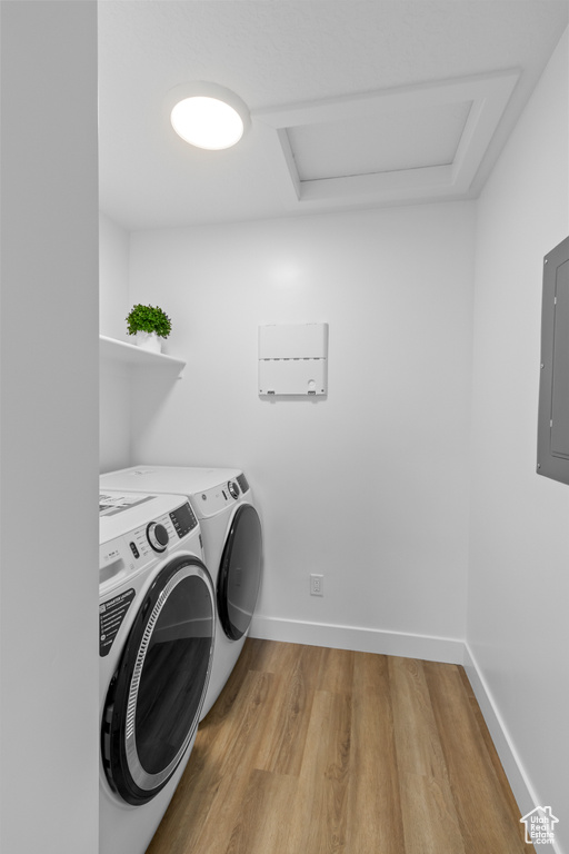 Laundry room with attic access, washing machine and dryer, light wood-style flooring, baseboards, and electric panel