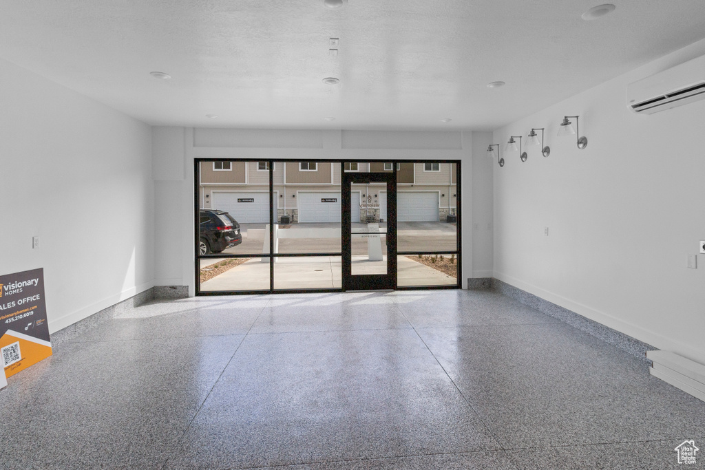 Empty room featuring speckle patterned floor, a wall mounted air conditioner, and baseboards