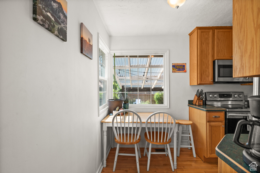 Kitchen featuring stainless steel appliances, light wood-style floors, brown cabinets, baseboards, and dark countertops