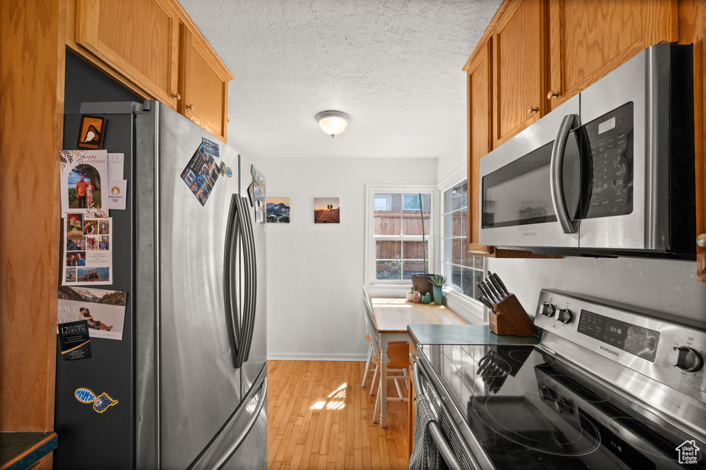Kitchen featuring appliances with stainless steel finishes, light wood-style flooring, a textured ceiling, baseboards, and brown cabinets