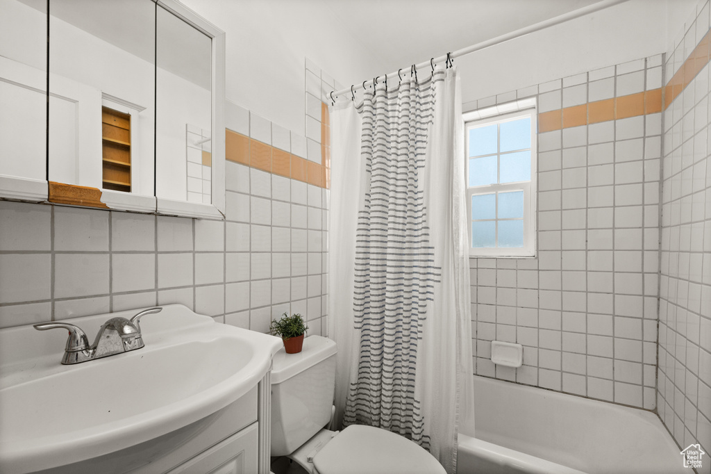 Full bathroom with tile walls, toilet, shower / tub combo with curtain, tasteful backsplash, and vanity