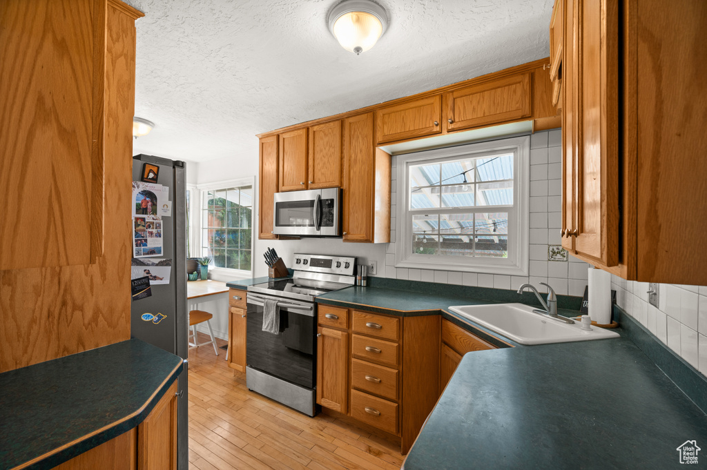 Kitchen with appliances with stainless steel finishes, a sink, a textured ceiling, brown cabinets, and dark countertops