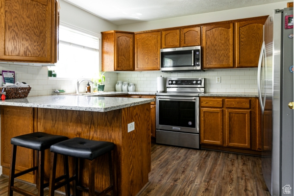 Kitchen with stainless steel appliances, dark wood-style floors, a peninsula, decorative backsplash, and a sink