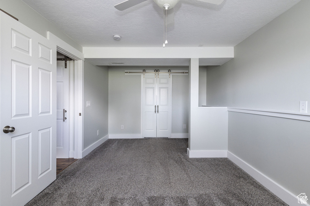 Unfurnished bedroom featuring a barn door, carpet floors, a textured ceiling, baseboards, and a closet